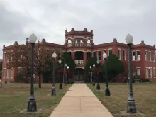 Red-brick historic building at the end of a lamp-lined walkway.